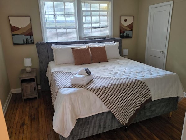 A bedroom with a bed, bedside tables, a door, and artwork on the walls. - Pershing Park Retreat (Montgomery)