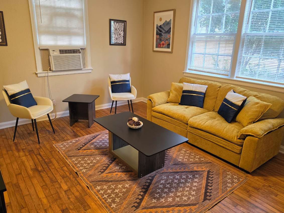 A living room with a yellow sofa, two armchairs, a coffee table, and patterned rugs.