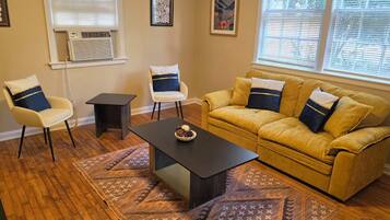 A living room with a yellow sofa, two armchairs, a coffee table, and patterned rugs.