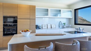 A modern kitchen with a central island, built-in appliances, and a view of the outdoors. - Villa Orizonte – Piscine à débordement et vue panoramique (Santa-Reparata-di-Balagna)