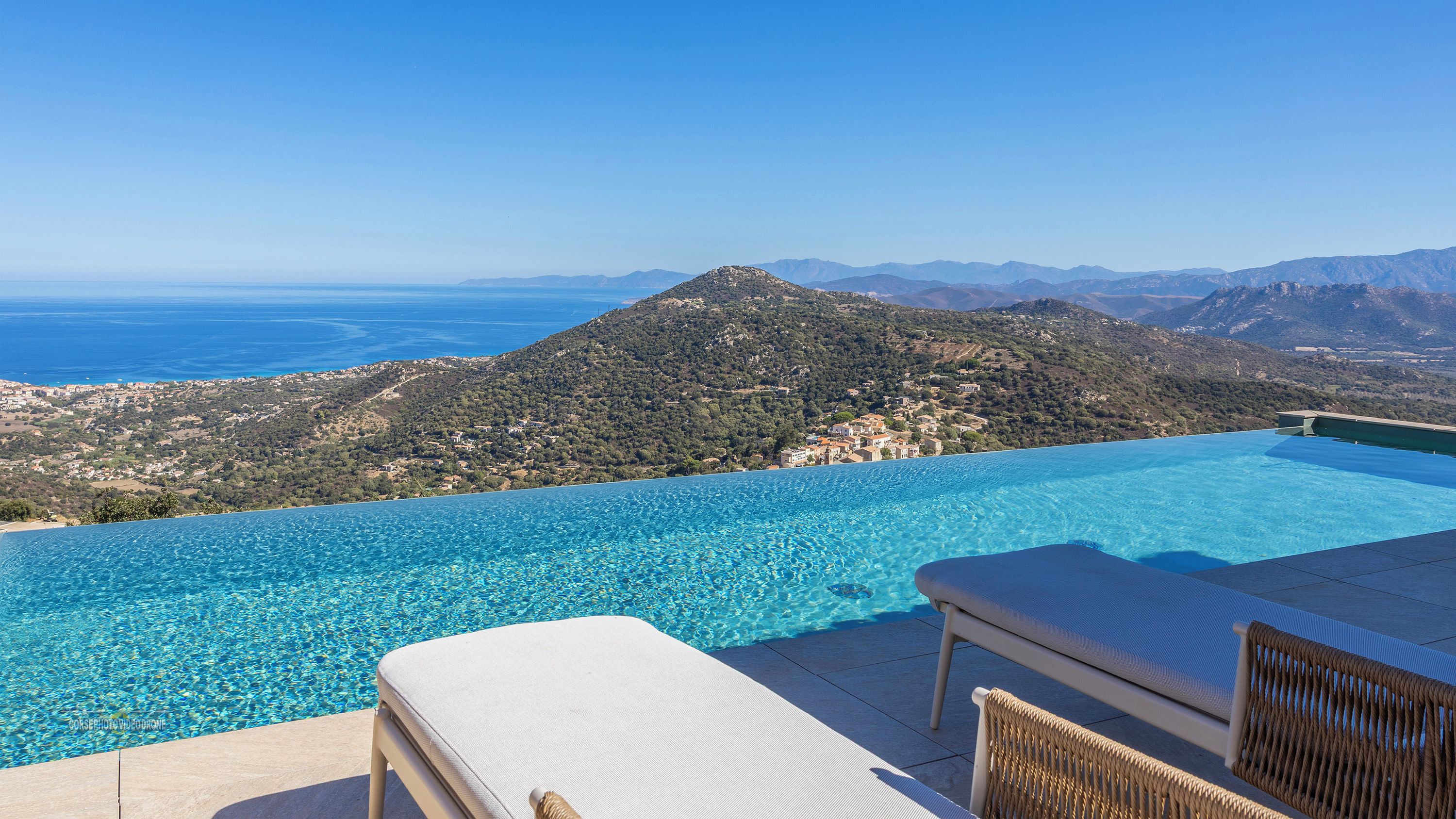Une piscine à débordement offrant une vue sur la mer et les montagnes.