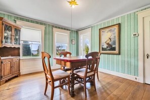 A dining area with a wooden table and chairs, a window with a view, and a painting on the wall. - Port Clyde Road (Tenants Harbor)