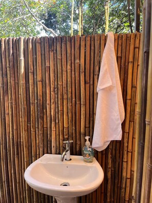 Ein Badezimmer mit Bambuswand, einem weißen Waschbecken, einem Wasserhahn und einer Seifenspender.