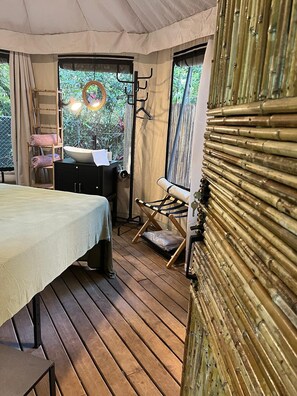 Ein Zeltraum mit einem Bett, einem kleinen Tisch, einem Stuhl und einer Kleiderstange.