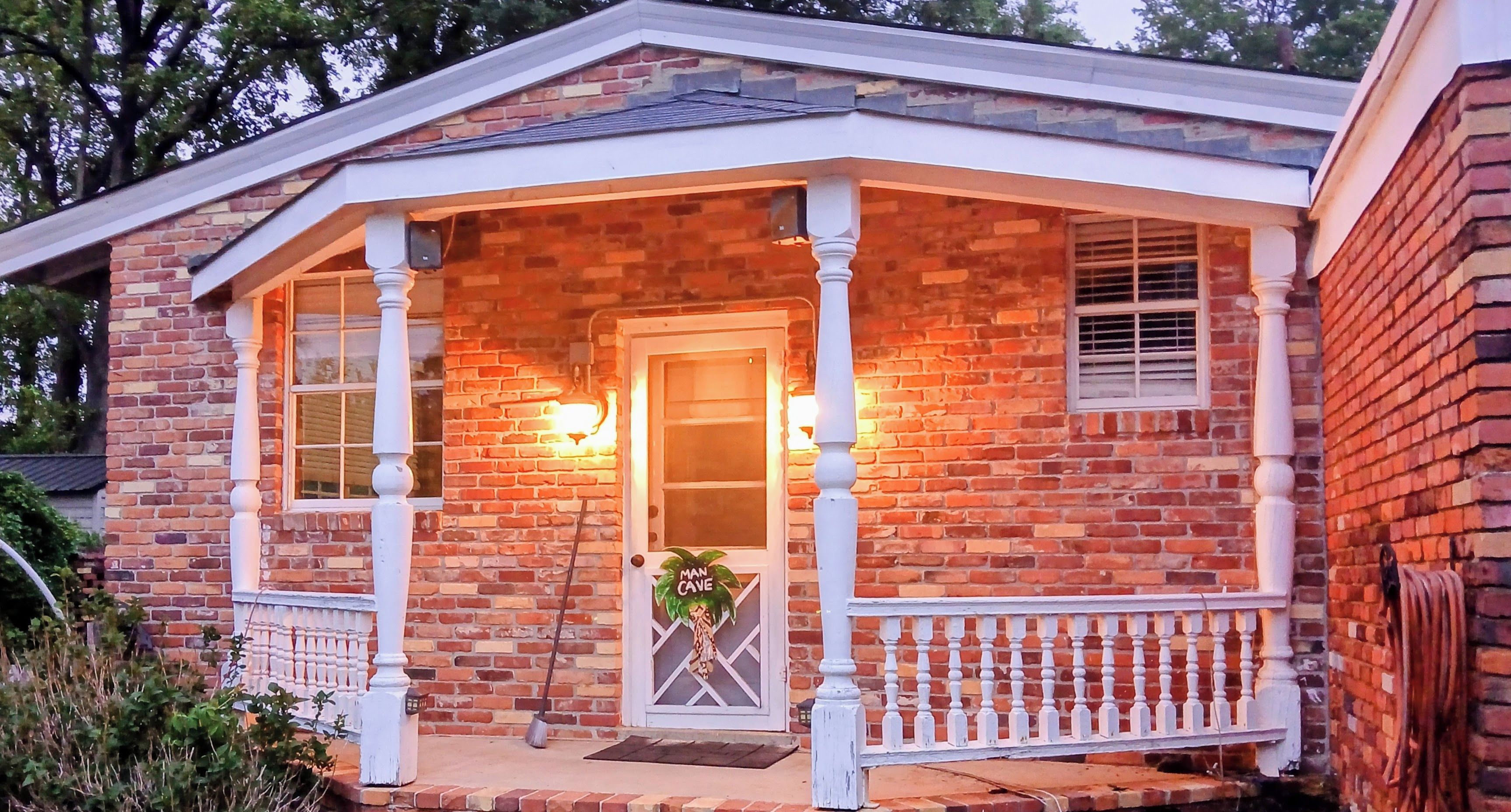 A brick house with a porch, a door with a palm tree decoration, and a small garden area.