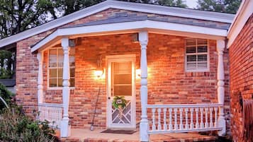 A brick house with a porch, a door with a palm tree decoration, and a small garden area.