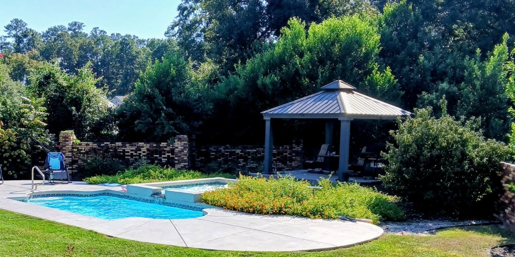 A backyard with a swimming pool, a gazebo, and a brick wall.