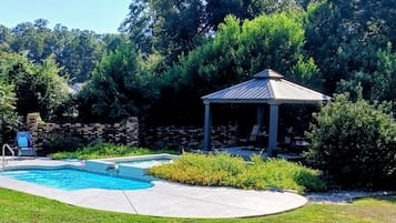 A backyard with a swimming pool, a gazebo, and a brick wall.