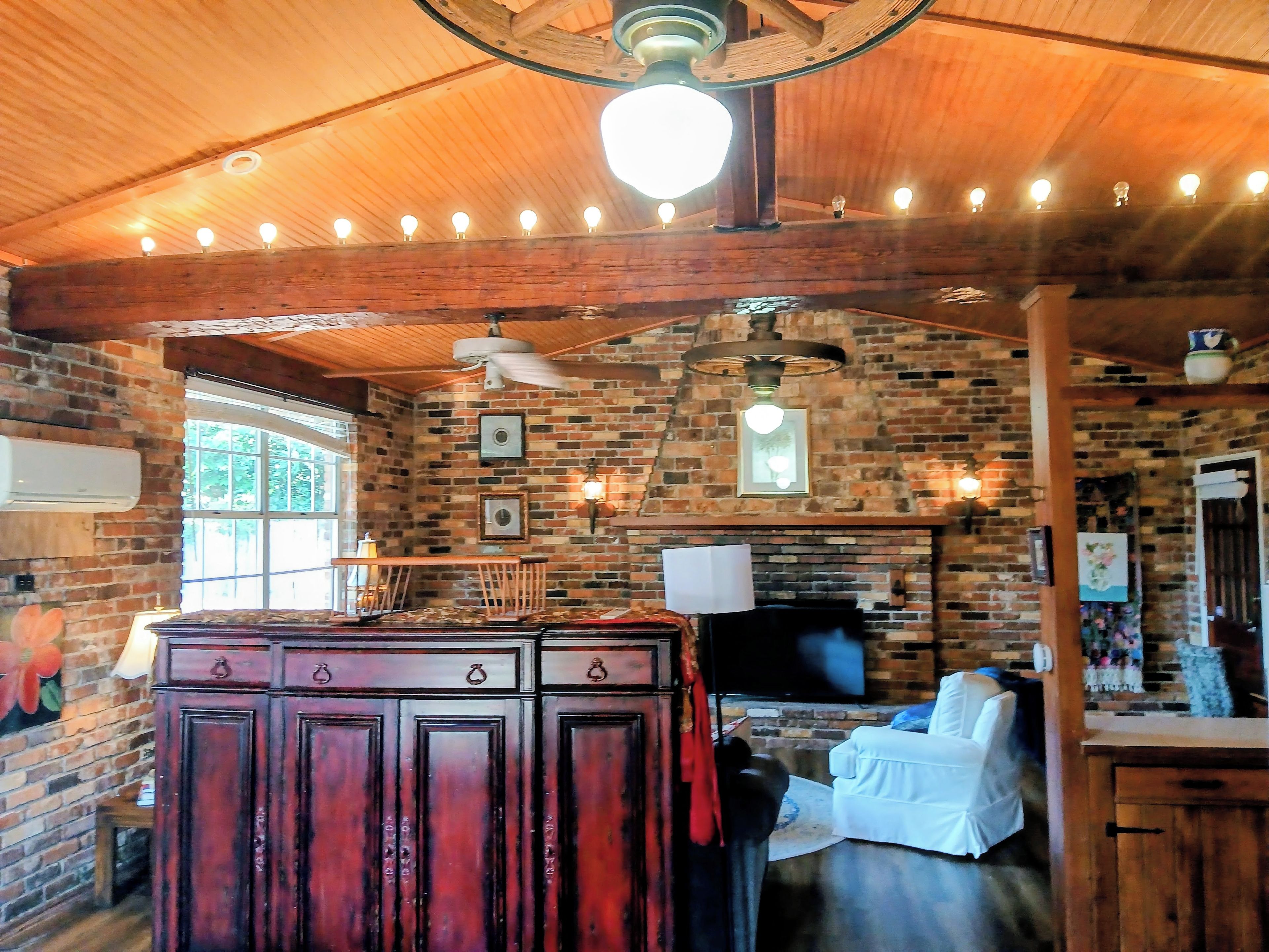A rustic interior with exposed brick walls, wooden beams, a central island with a flat-screen TV, and a ceiling fan.