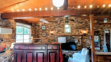 A rustic interior with exposed brick walls, wooden beams, a central island with a flat-screen TV, and a ceiling fan.