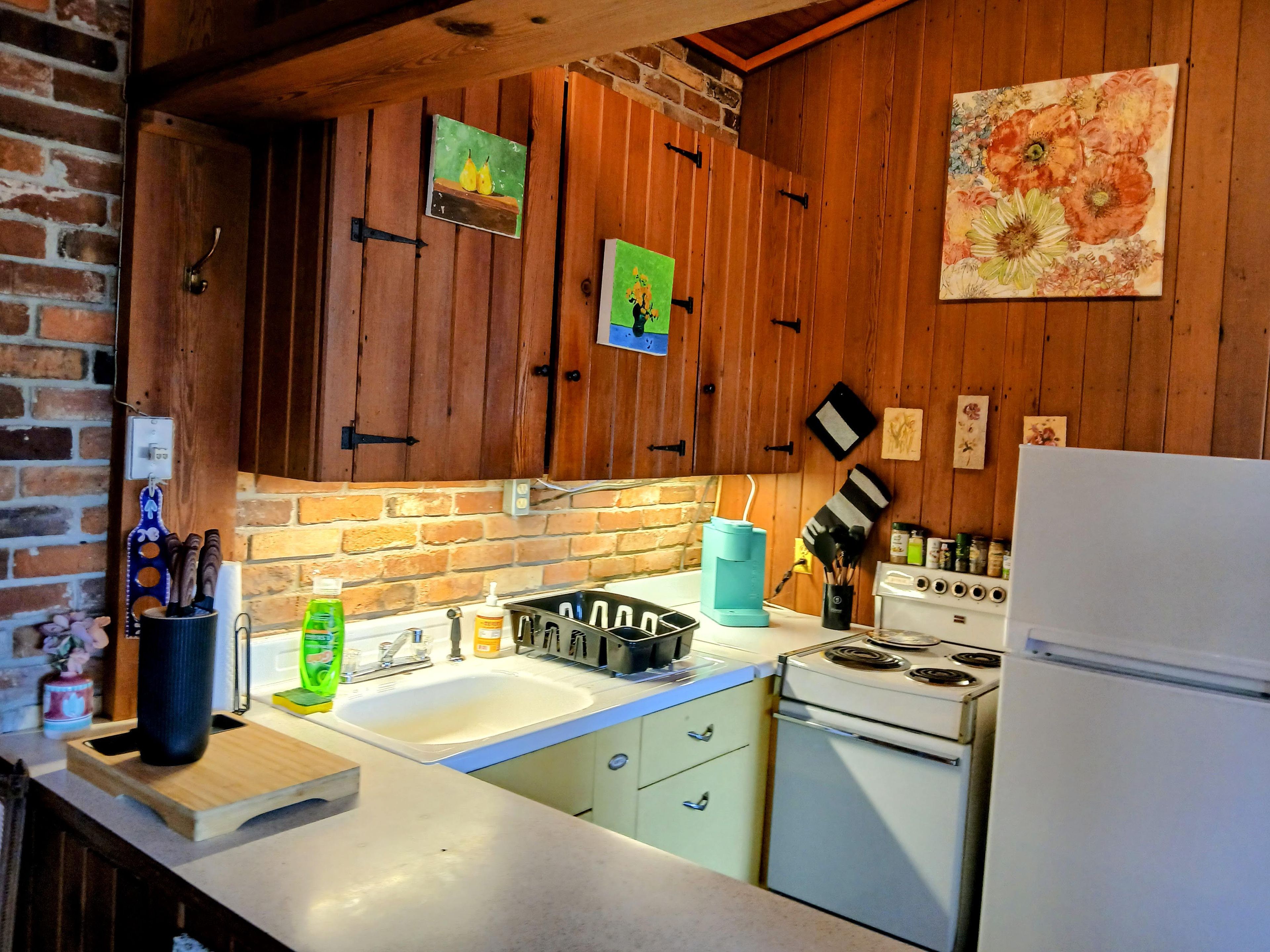 Une cuisine avec des meubles de rangement en bois, un évier, une cuisinière et un réfrigérateur.