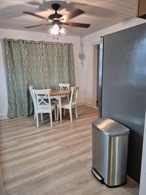 A dining area with a table and chairs, a ceiling fan, and a trash bin. - Almosta Beach House  in Clearwater (Clearwater)
