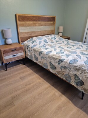 Une chambre à coucher avec une tête de lit en bois, un lit recouvert d’une couvre-lit à motifs, une table de chevet avec des tiroirs et une lampe de chevet.