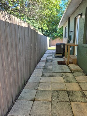 A narrow concrete pathway leading to a building with a wooden fence on one side and a green wall on the other. - Almosta Beach House  in Clearwater (Clearwater)