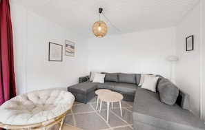A modern living room with a grey sectional sofa, a white cushioned chair, and a hanging light fixture. - 4 bedroom beautiful home in Hvide Sande (Hvide Sande)