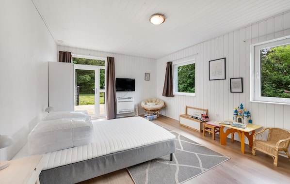 Une chambre avec un lit, une télévision, un bureau avec des jouets et une vue sur la verdure à l’extérieur.