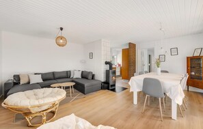 Un salon moderne avec un canapé, une table à manger et des chaises, un fauteuil en osier et une cheminée.