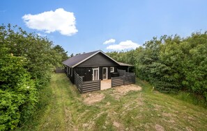 Une petite cabane en bois à la couleur sombre, dotée d’un toit en pente et entourée d’une végétation luxuriante.