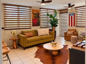 A living room with a sofa, a coffee table, a plant, and a flag. - Ocean Views | 2 King Beds, Pool & Beach Gear (Rincón)