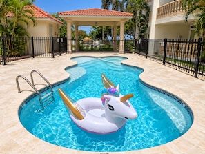 A swimming pool with a unicorn float, a covered seating area, and a black fence surrounding the property. - Ocean Views | 2 King Beds, Pool & Beach Gear (Rincón)