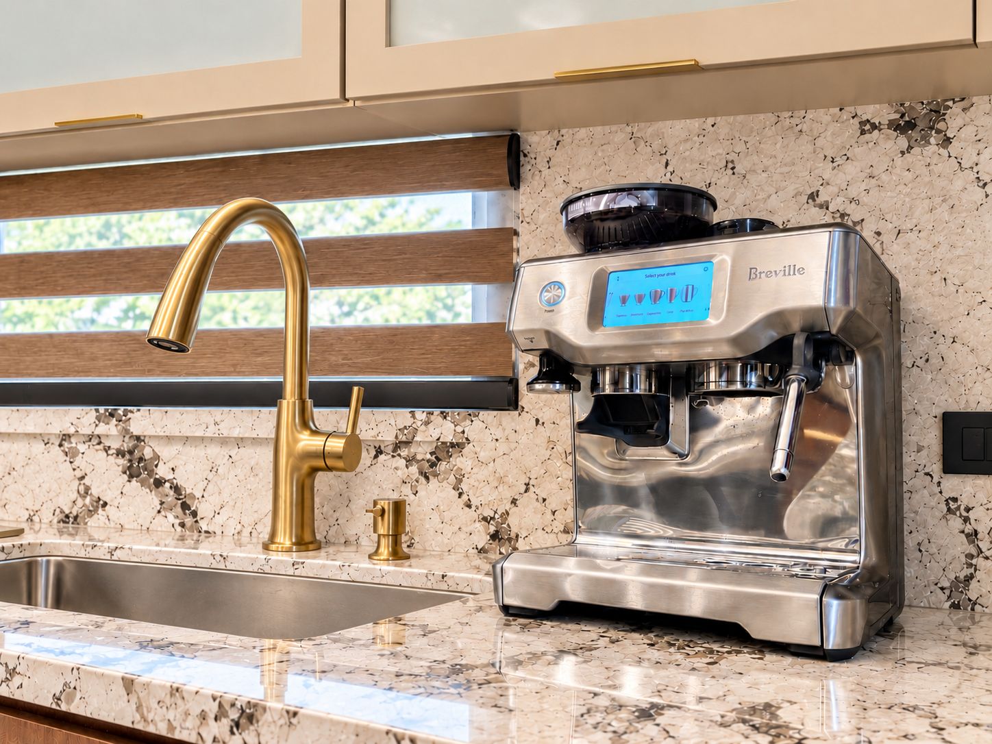 Een keuken met een Breville espressomachine, een gouden kraan en een granieten aanrecht.