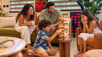 Een gezin speelt Jenga in een gezellige woonkamer met een groene bank, een bijzettafeltje en een decoratieve lamp.