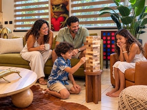 A family playing Jenga in a cozy living room with a green sofa, a coffee table, and a decorative lamp. - Ocean Views | 2 King Beds, Pool & Beach Gear (Rincón)