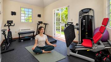 A gym with exercise equipment, a seated person meditating, and a view of greenery outside.