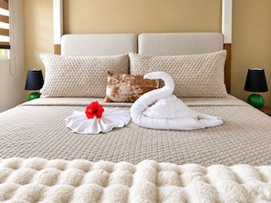 A bed with a quilted headboard, a swan-shaped pillow, a red flower, and two lamps on nightstands. - Ocean Views | 2 King Beds, Pool & Beach Gear (Rincón)