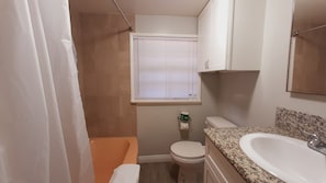 Ein Badezimmer mit Dusche, Toilette, Waschbecken und Fenster mit Jalousien.