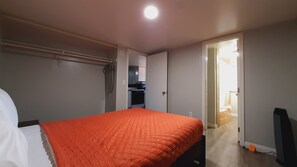 A bedroom with a bed, a wardrobe, and a kitchenette in the background. - SHERWOOD ARMS MOTEL _CABIN #6 (Running Springs)