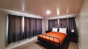 Un dormitorio con una cama, cortinas, una mesita de noche y una lámpara.