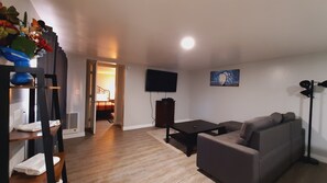 A living room with a sofa, a coffee table, a flat-screen TV mounted on the wall, and a wooden floor. - SHERWOOD ARMS MOTEL _CABIN #6 (Running Springs)