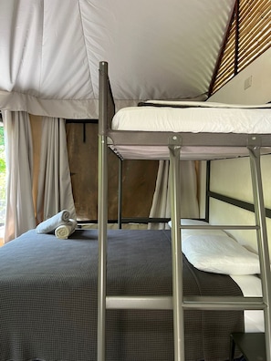 A bunk bed with a mattress and pillows, a rolled towel, and a window with curtains.