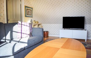 A living room with a grey sofa, a wooden coffee table, a white TV stand, and patterned wallpaper. - Stunning home in Sättra with WiFi (Sättra)