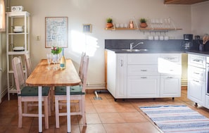 A kitchen with white cabinets, a wooden dining table with chairs, a tiled floor, and a kitchen island with a sink. - Stunning home in Sättra with WiFi (Sättra)