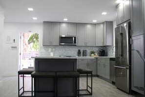 A modern kitchen with grey cabinets, a stainless steel refrigerator, and a bar stool area.