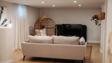 A modern living room with a sofa, a hanging chair, a flat-screen TV, and a wall-mounted plant.