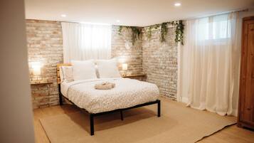 Une chambre avec un mur en briques, un lit recouvert d’une couvre-lit à motifs floraux, deux lampes de chevet et une fenêtre avec des rideaux.