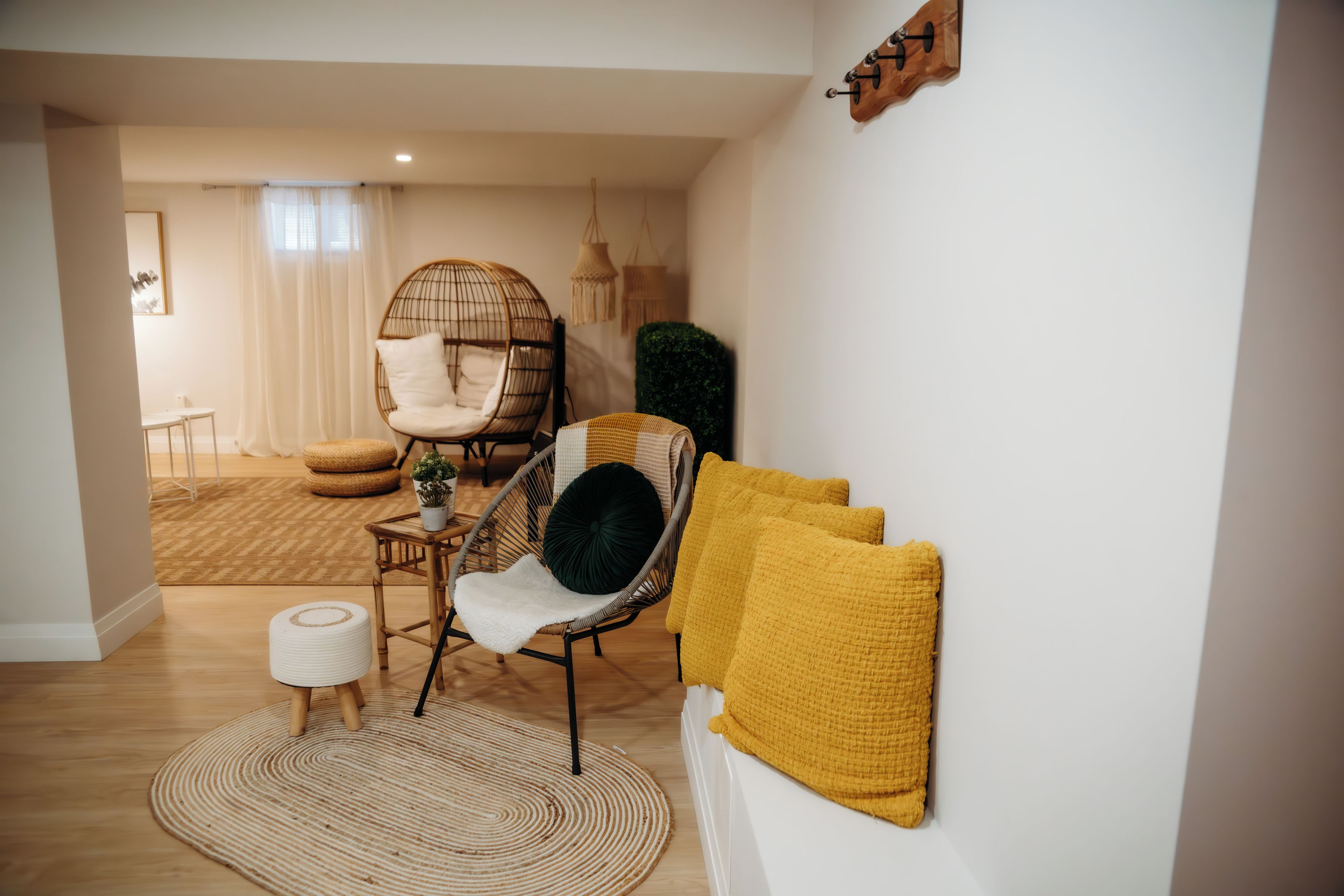 Una sala moderna con un sillón redondo de mimbre, un sofá con cojines amarillos y una alfombra tejida.