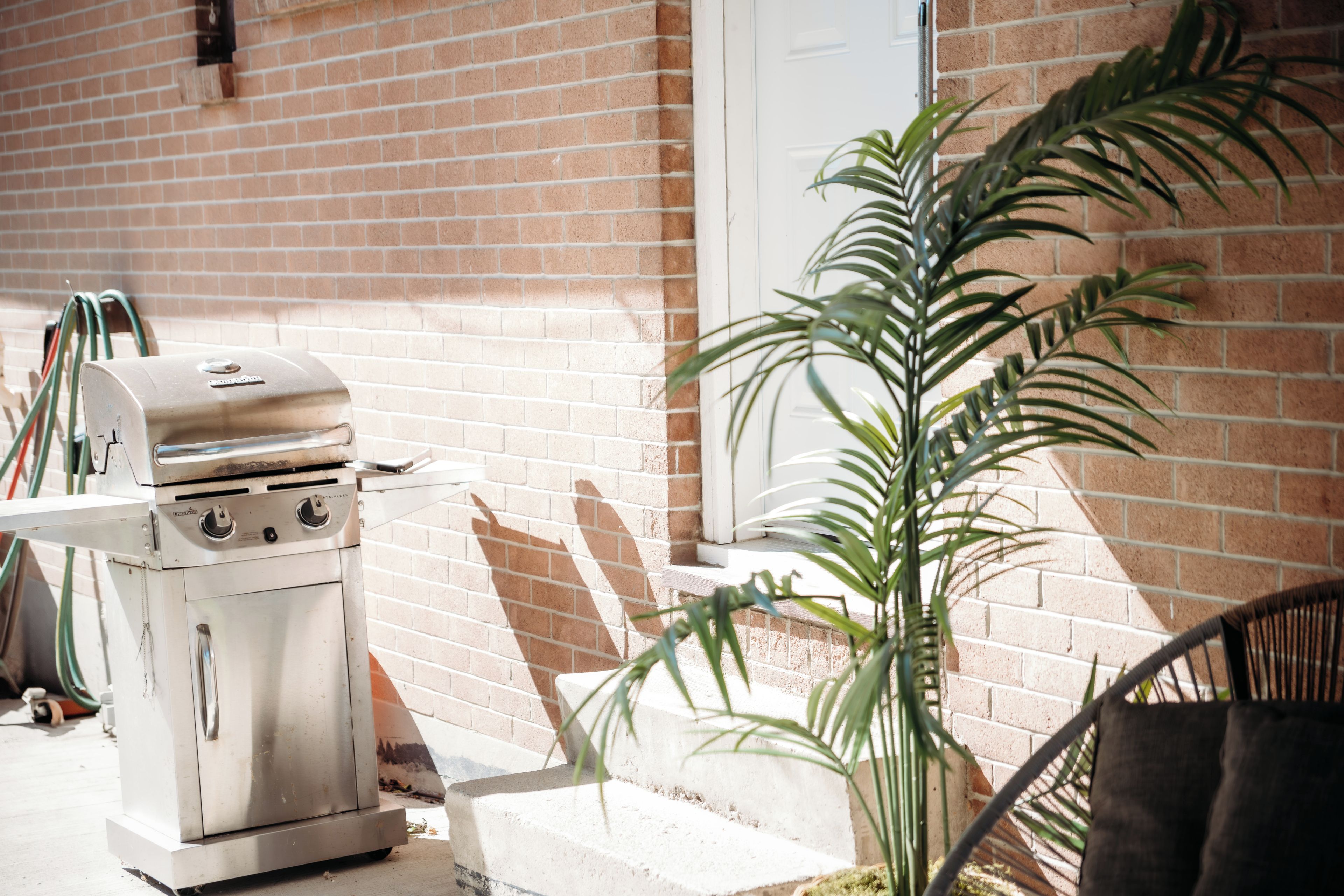 A stainless steel grill with a control panel, hoses, and a brick wall in the background.