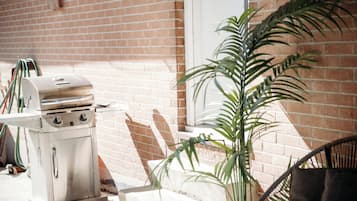 A stainless steel grill with a control panel, hoses, and a brick wall in the background.