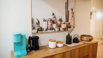 Un piano di lavoro in cucina con una macchina per il caffè, bollitori e barattoli, un armadietto di legno e una parete decorata con cactus.