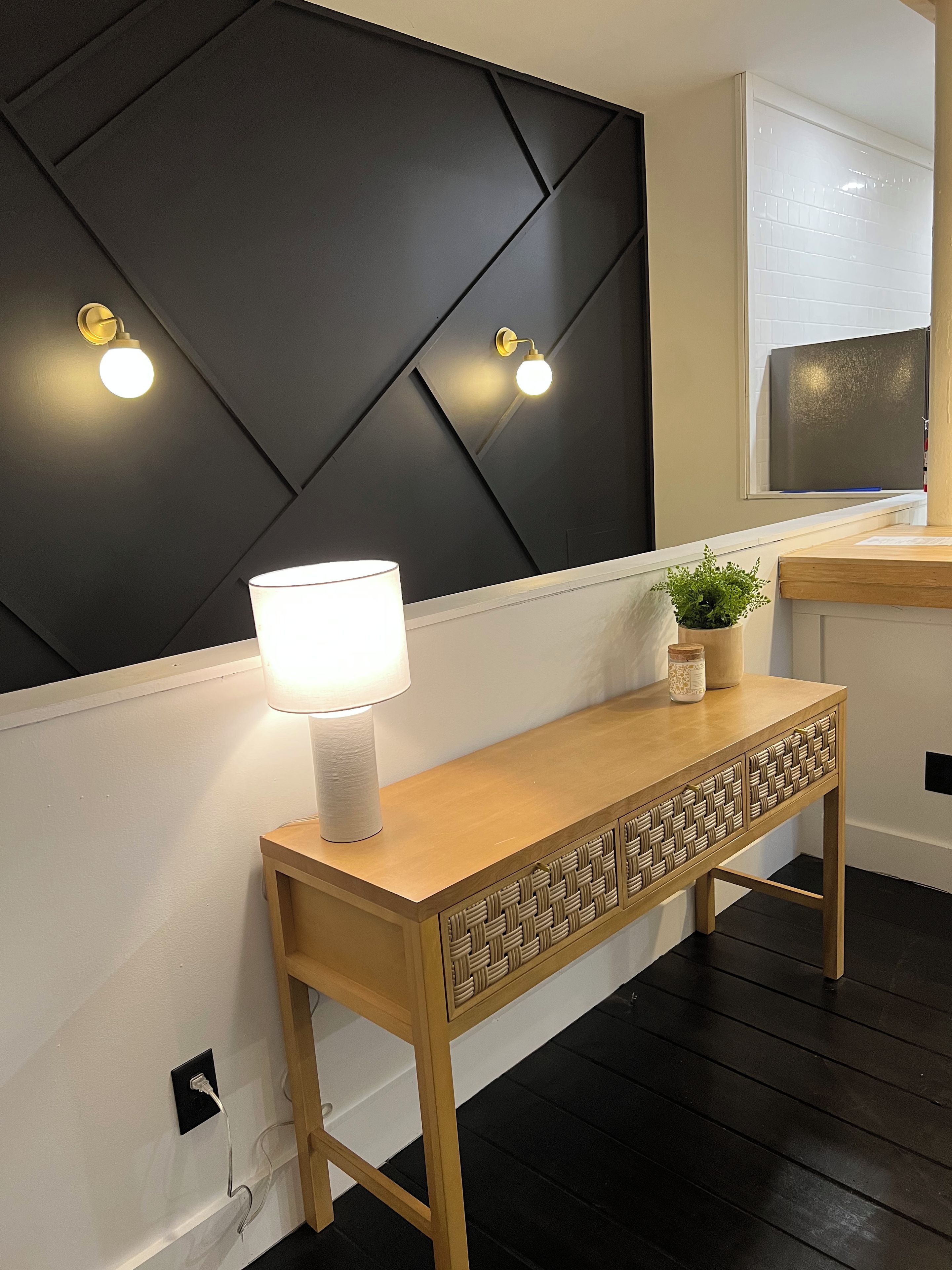 Una habitación moderna con una pared de acento oscura, una mesita de consola de madera con una lámpara y una planta en maceta.