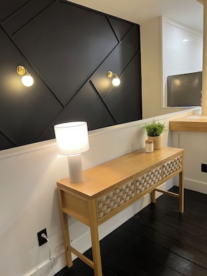 Una habitación moderna con una pared de acento oscura, una mesita de consola de madera con una lámpara y una planta en maceta.