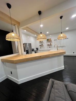 Una cocina moderna con una isla central, luces colgantes y suelo negro.