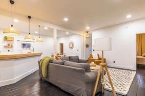 Una sala de estar moderna con un sofá gris, suelo de madera y un comedor con mesa y sillas de madera.