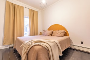 Ein Schlafzimmer mit einem großen Bett, cremefarbenen Vorhängen, einer geometrischen Deckenleuchte und Blick ins Freie.