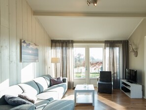 Ein Wohnzimmer mit einer Couch, einem Couchtisch, einem Fernseher und Blick durch die Glastür.