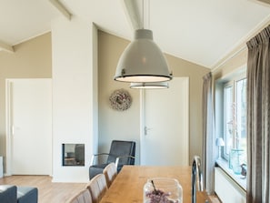A dining area with a wooden table, chairs, a pendant light, a fireplace, and a view of the outdoors through a window. - Charming Bungalow on Ameland With a Beautiful Garden (Hollum)